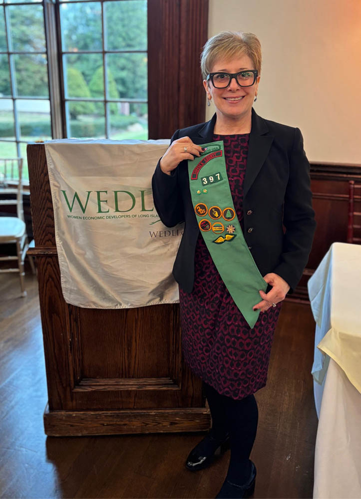 Debra Thompson posing in front of WEDLI podium holding a girl scout banner
